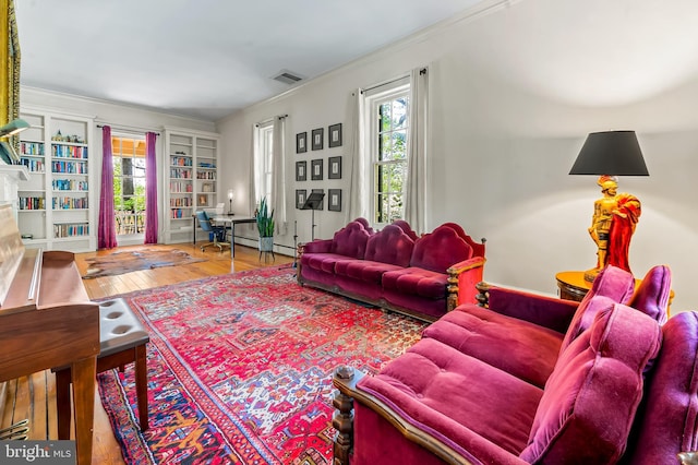 living area with built in features, visible vents, ornamental molding, and wood finished floors