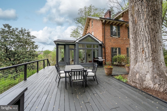 wooden deck with a sunroom, outdoor dining area, and a grill