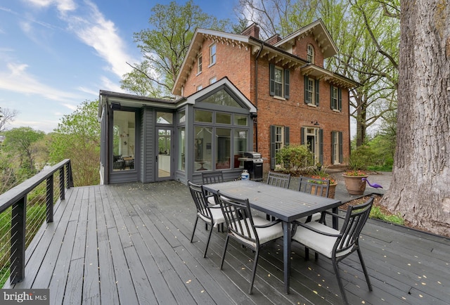 wooden deck featuring area for grilling, outdoor dining space, and a sunroom