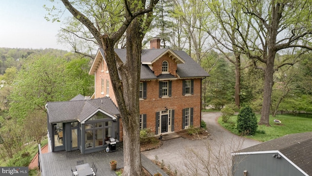 view of front of property featuring roof with shingles, brick siding, a chimney, a patio area, and a wooded view