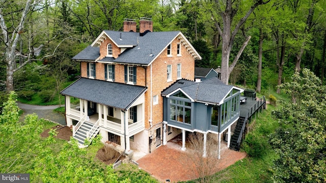 rear view of house with a porch, driveway, a chimney, roof with shingles, and stairway
