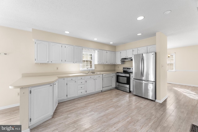 kitchen with a peninsula, appliances with stainless steel finishes, a sink, and light wood-style floors