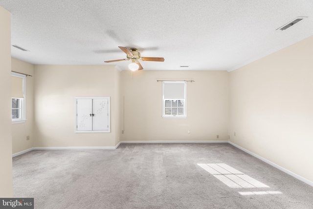 carpeted spare room with a textured ceiling, baseboards, a ceiling fan, and visible vents