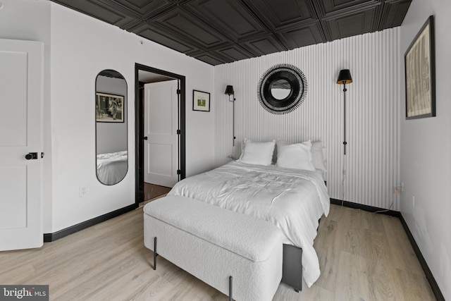 bedroom with light wood-style floors, an ornate ceiling, and baseboards