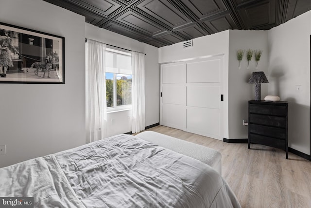 bedroom featuring a closet, an ornate ceiling, light wood-type flooring, and baseboards