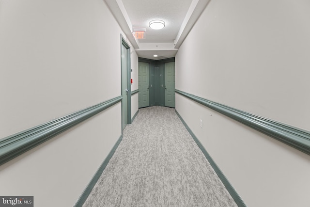 hall featuring light carpet, a textured ceiling, and baseboards