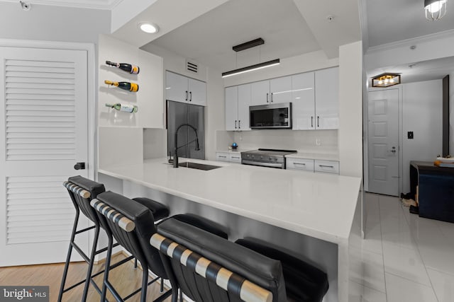 kitchen featuring a kitchen breakfast bar, a peninsula, white cabinets, stainless steel appliances, and a sink