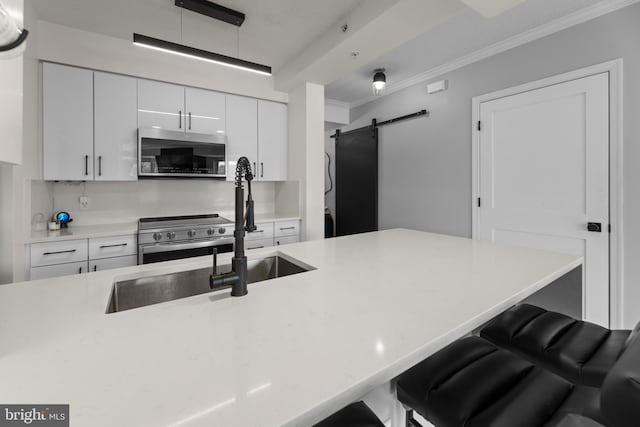 kitchen featuring a barn door, ornamental molding, appliances with stainless steel finishes, a breakfast bar, and white cabinetry