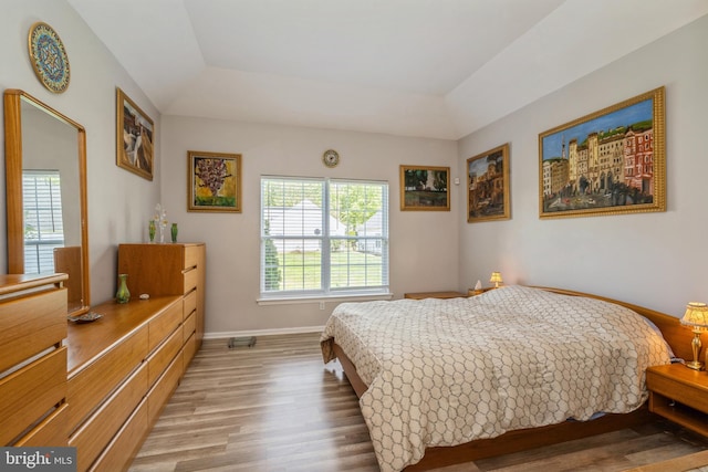 bedroom with light wood-style floors, a raised ceiling, and baseboards