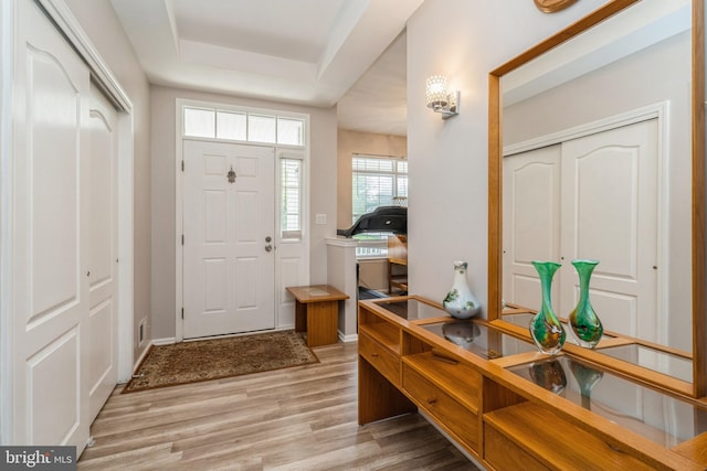 entryway with light wood-type flooring, a tray ceiling, and baseboards