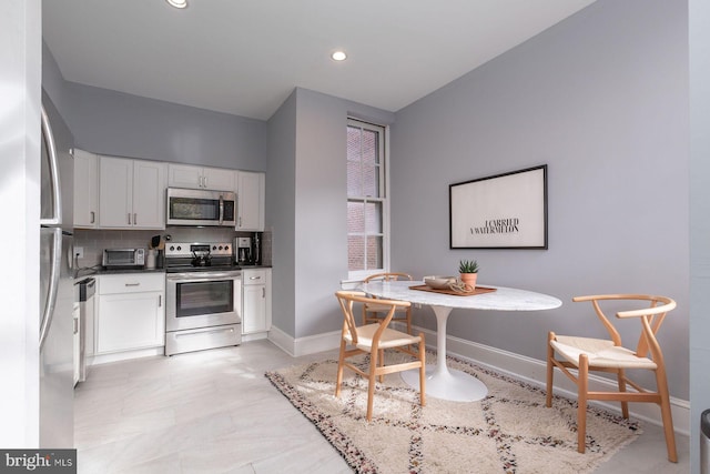 kitchen featuring dark countertops, decorative backsplash, white cabinets, baseboards, and appliances with stainless steel finishes