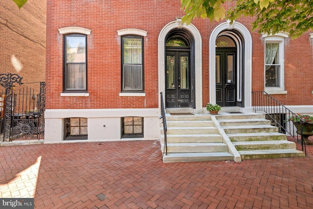 entrance to property featuring brick siding, french doors, and fence