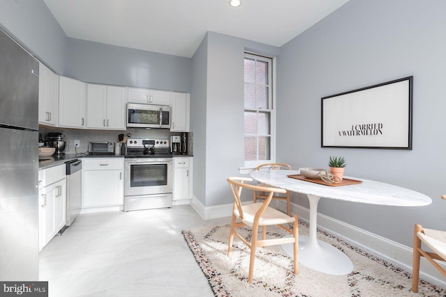 kitchen featuring stainless steel appliances, dark countertops, baseboards, tasteful backsplash, and white cabinetry