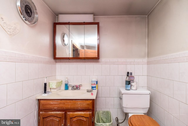 bathroom with wainscoting, tile walls, vanity, and toilet
