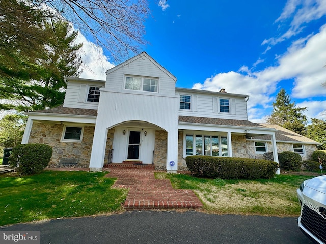 traditional-style house featuring roof with shingles, a chimney, a front lawn, and stone siding