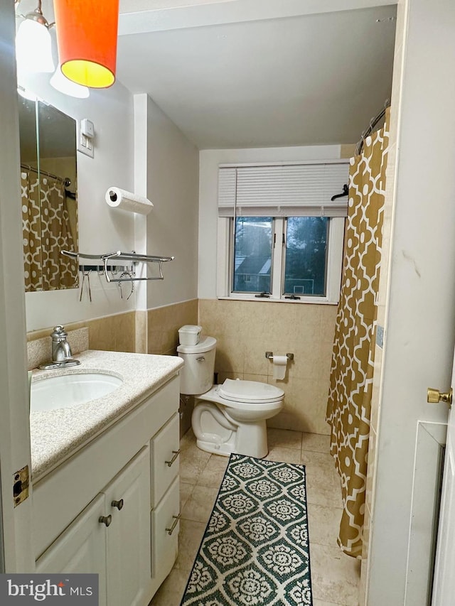 full bath featuring tile patterned floors, wainscoting, tile walls, toilet, and vanity