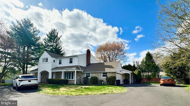 view of front of property with a chimney, aphalt driveway, a front lawn, and stone siding