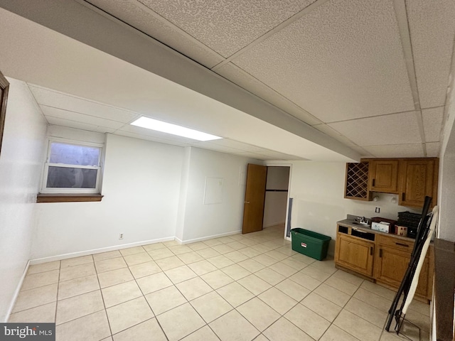 interior space featuring light tile patterned floors, a paneled ceiling, brown cabinetry, and baseboards