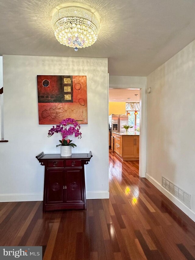 hall with dark wood-type flooring, a notable chandelier, baseboards, and visible vents