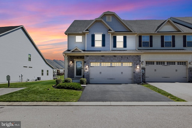 view of property featuring roof with shingles, stone siding, a garage, aphalt driveway, and a yard