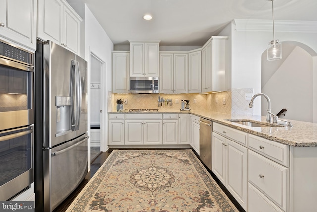 kitchen with a sink, stainless steel appliances, a peninsula, white cabinetry, and tasteful backsplash