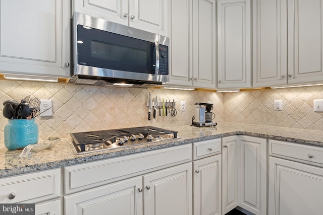 kitchen with appliances with stainless steel finishes, light stone counters, backsplash, and white cabinetry