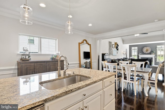 kitchen with a healthy amount of sunlight, hanging light fixtures, a sink, open floor plan, and ornamental molding