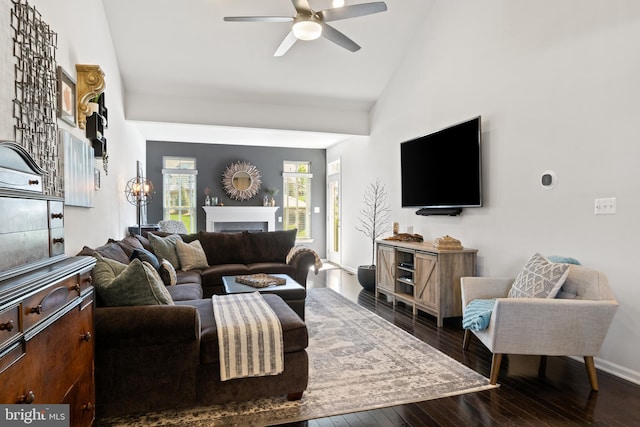 living room featuring a ceiling fan, a fireplace, vaulted ceiling, baseboards, and dark wood-style floors