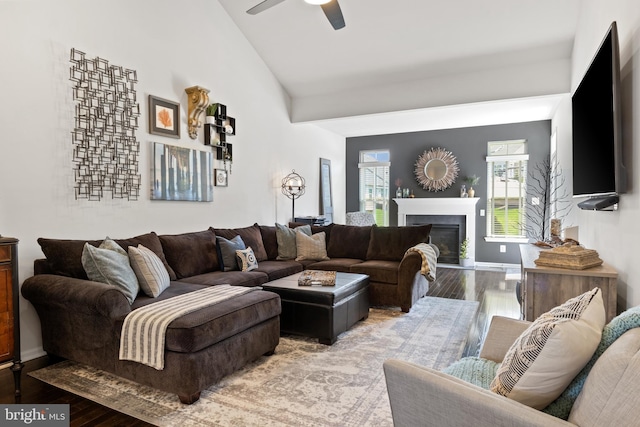 living room with a glass covered fireplace, wood finished floors, lofted ceiling, baseboards, and ceiling fan