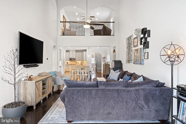 living area with dark wood-style flooring, a towering ceiling, ceiling fan, recessed lighting, and arched walkways