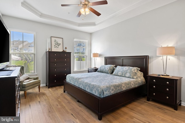 bedroom featuring a ceiling fan, baseboards, light wood finished floors, ornamental molding, and a tray ceiling