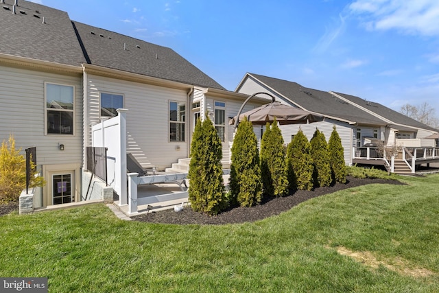 rear view of house featuring a lawn, a wooden deck, and a shingled roof