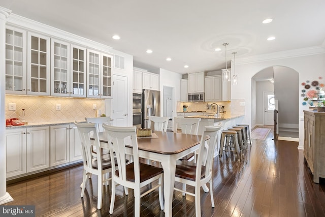 dining area with crown molding, arched walkways, recessed lighting, and dark wood finished floors