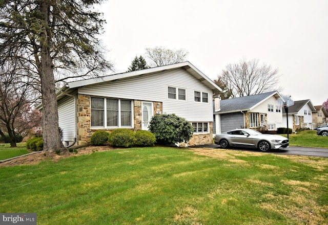 split level home featuring a front lawn, driveway, and stone siding