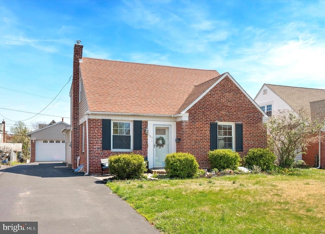 view of front facade featuring a front lawn, a chimney, brick siding, and a detached garage