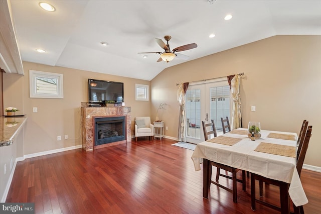 dining area with a ceiling fan, hardwood / wood-style flooring, a tile fireplace, baseboards, and lofted ceiling