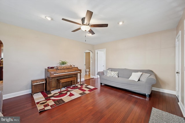living area with arched walkways, wood-type flooring, and a ceiling fan