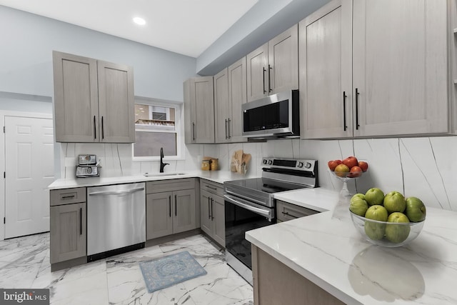 kitchen with recessed lighting, light stone countertops, gray cabinetry, appliances with stainless steel finishes, and a sink