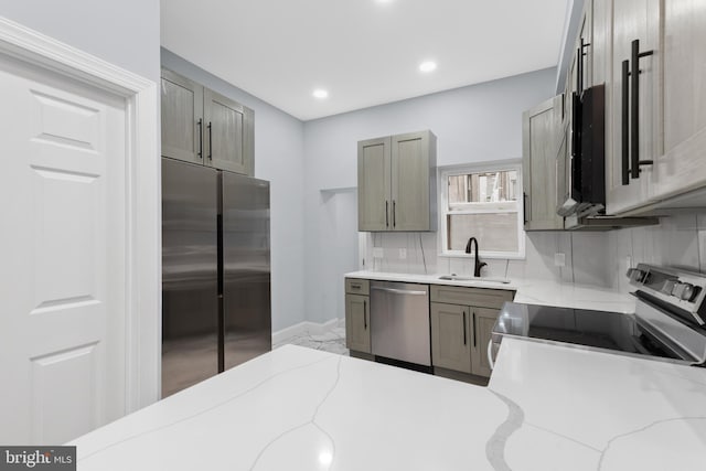 kitchen featuring baseboards, appliances with stainless steel finishes, a sink, and light stone countertops