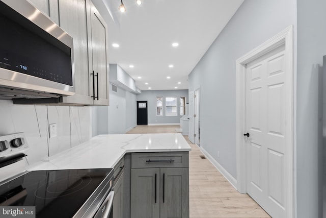 kitchen with light stone countertops, a peninsula, gray cabinets, appliances with stainless steel finishes, and light wood finished floors