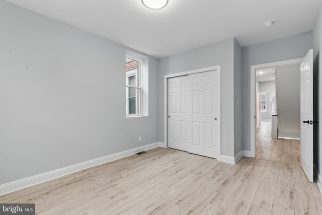 unfurnished bedroom with a closet, baseboards, and light wood-style floors