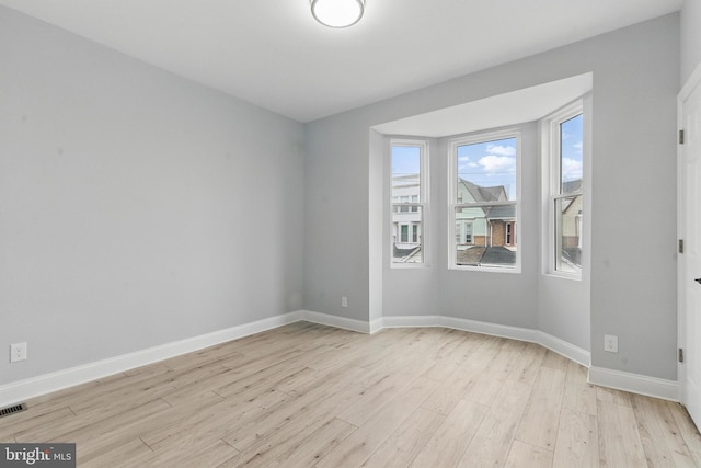 spare room featuring visible vents, light wood finished floors, baseboards, and plenty of natural light