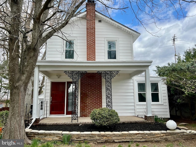 view of front facade featuring brick siding, a chimney, and covered porch