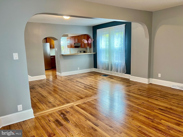 unfurnished living room featuring arched walkways, wood finished floors, visible vents, and a wealth of natural light