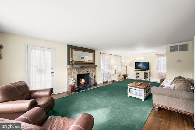 living area with wood finished floors, baseboards, a stone fireplace, and visible vents