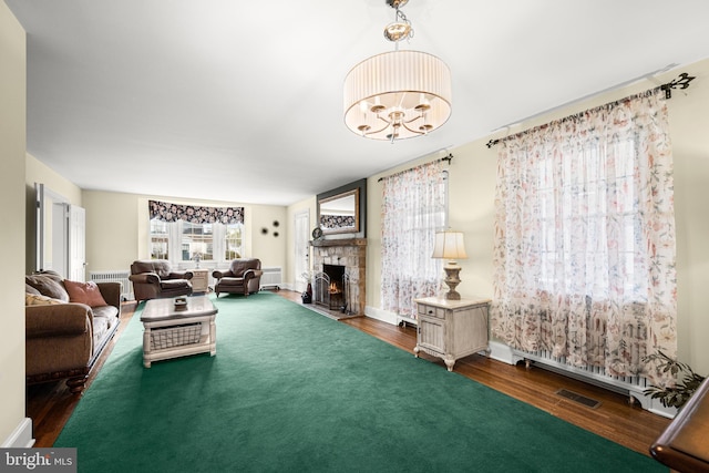 living area with radiator heating unit, a stone fireplace, and wood finished floors