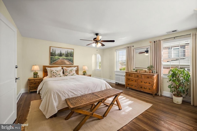 bedroom with dark wood-style flooring, arched walkways, radiator, baseboards, and visible vents