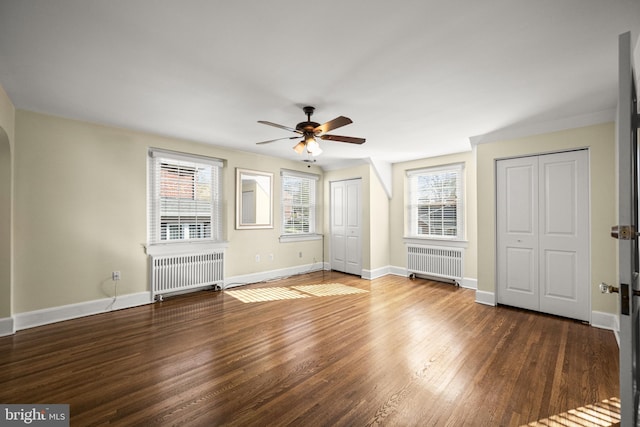 unfurnished bedroom with radiator heating unit, baseboards, two closets, and wood finished floors