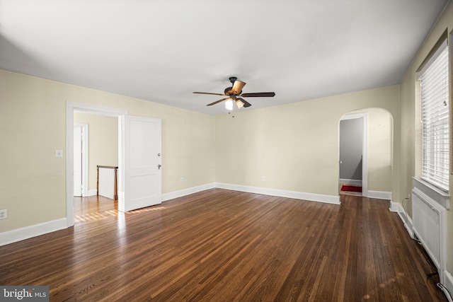unfurnished living room with arched walkways, ceiling fan, dark wood finished floors, and baseboards