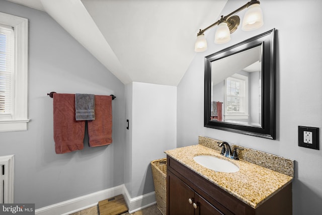 bathroom featuring baseboards, vanity, vaulted ceiling, and a healthy amount of sunlight